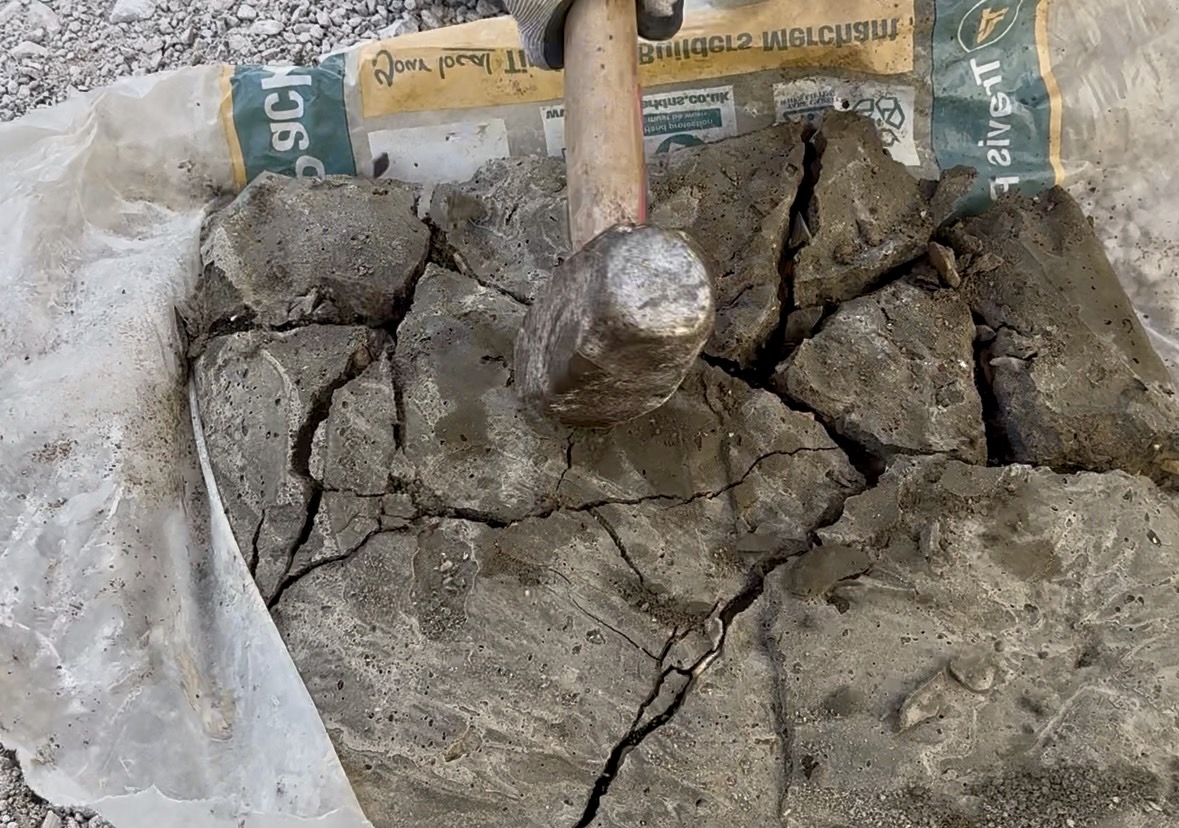 Breaking a flattened slab of leftover concrete with a club hammer after it was bagged and left to set the day before.