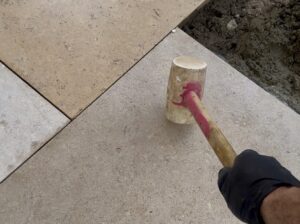 Rubber mallet knocking down a paving slab while laying a patio.